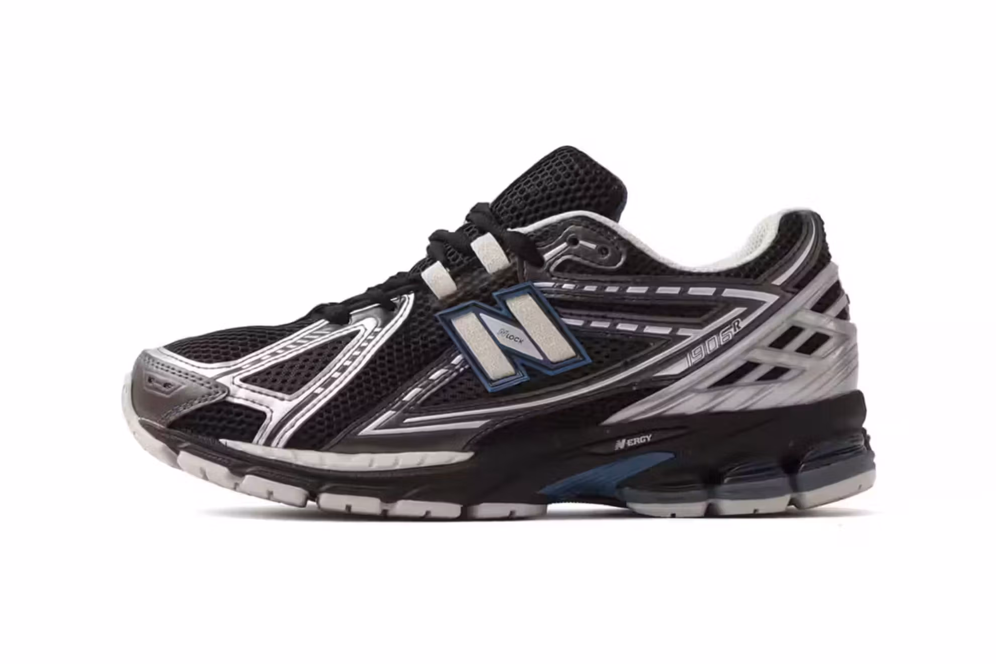 one side New Balance 1906R “Blue Moon” shoe in collaboration with atmos, featuring layered navy and gradient blue mesh, reflective metallic heel counters, and tonal blue accents, displayed on a textured grey stone surface with soft natural lighting highlighting the shoe’s atmospheric color palette