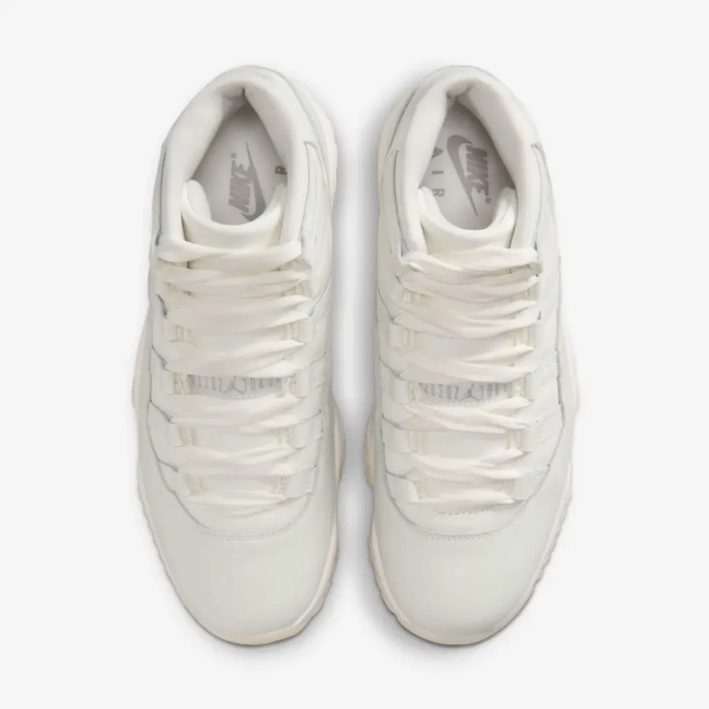 Top-down view of the Air Jordan 11 WMNS “Pearl” sneakers, highlighting the silky white laces, pearlescent patent leather mudguard, and soft champagne-toned upper on a clean white background