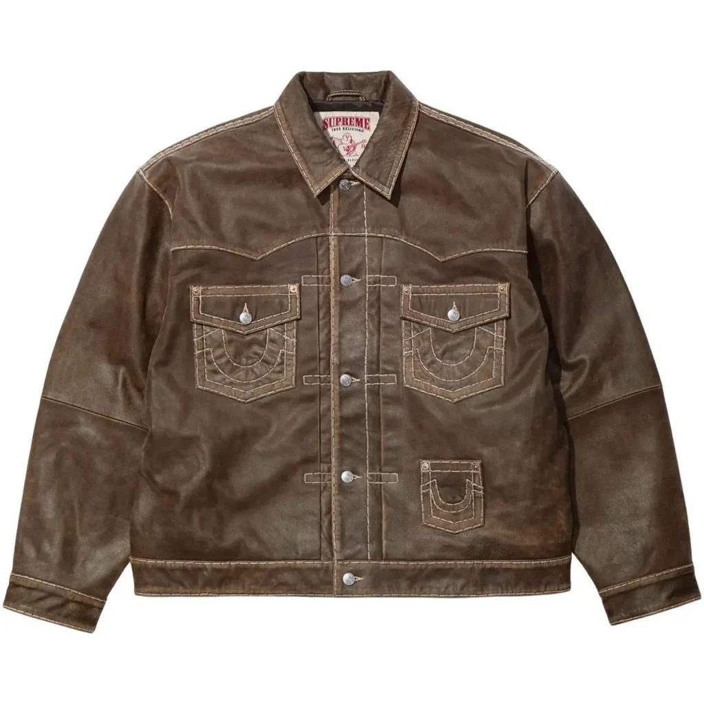A brown Supreme × True Religion leather trucker jacket featuring heavy contrast stitching, multiple horseshoe-stitched flap pockets, metal snap buttons, and a co-branded interior label at the collar