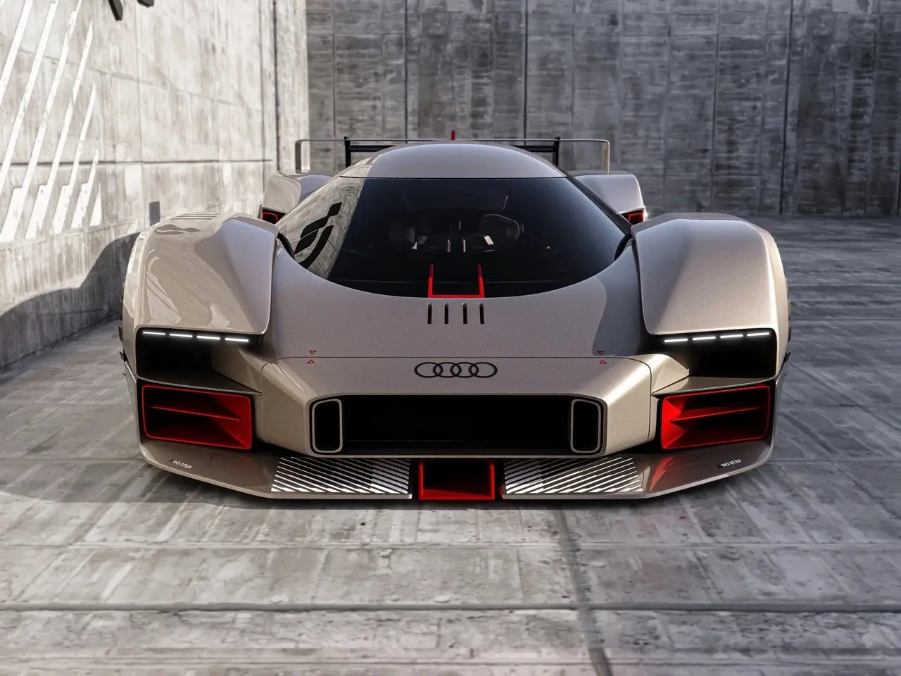 Front view of the Audi 20quattro Vision GT concept car showcasing its aggressive aerodynamic design, wide stance, illuminated Audi rings, and sharp LED headlight strips, with red aerodynamic accents and angular air intakes set against a concrete racing environment.