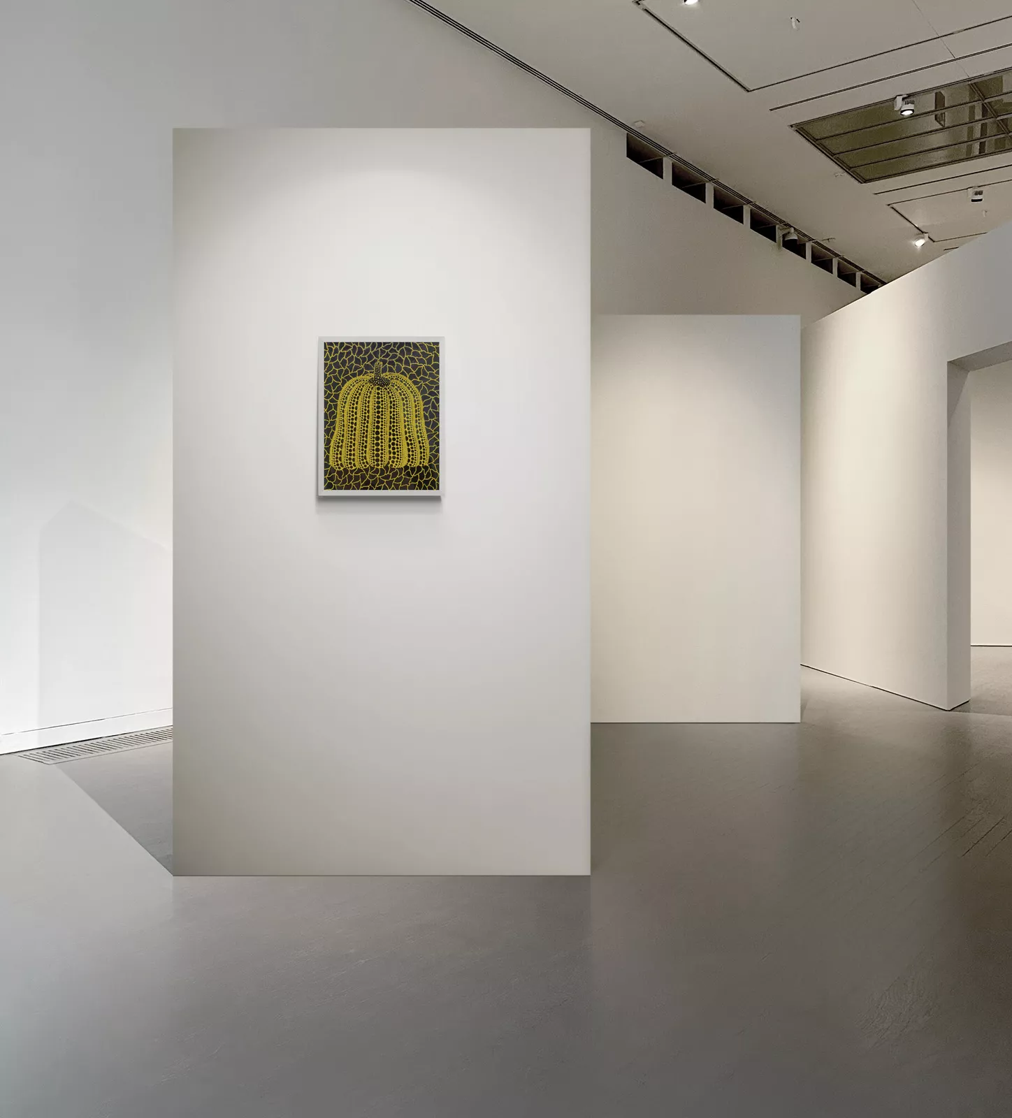 “Yayoi Kusama’s Pumpkin (1990) — a small yellow pumpkin covered in black dots and set against a crackled black-and-yellow background, displayed alone on a white wall inside Akunst Gallery’s minimalist, softly lit exhibition space.”