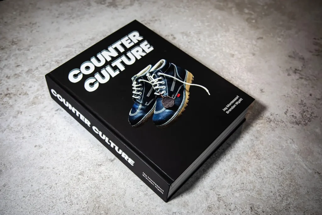 Hardcover copy of Counter Culture by Jay Montessori and Brendan Wyatt resting on a textured concrete surface, featuring a black cover with white bold title text and an image of blue Kickers boots at the center