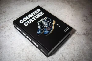 Hardcover copy of Counter Culture by Jay Montessori and Brendan Wyatt resting on a textured concrete surface, featuring a black cover with white bold title text and an image of blue Kickers boots at the center