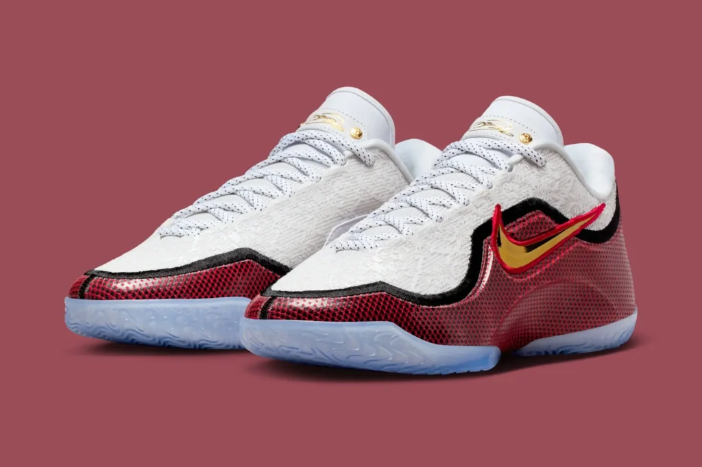 Front angle view of the Nike LeBron 23 “Grand Opening” basketball shoes featuring a white jacquard upper with embossed lion-mane texture, metallic gold Swoosh outlined in red, black contouring, and icy translucent sole set against a deep burgundy background.