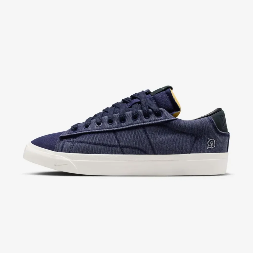 Side profile of a navy blue low-top sneaker featuring a minimalist canvas upper, tonal laces, a white midsole, and subtle branding near the heel