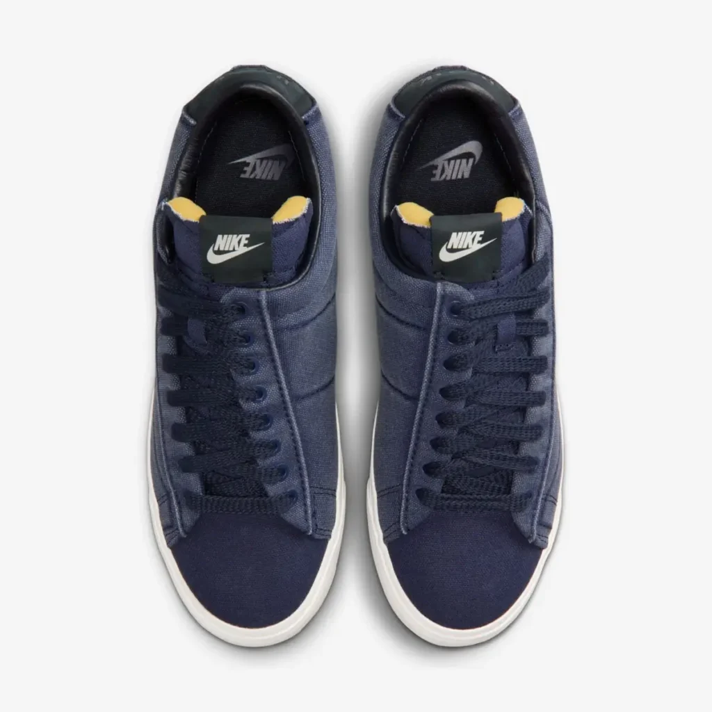 Top-down view of a pair of navy blue low-top Nike sneakers, showcasing the canvas upper, navy laces, exposed foam tongue edges, and white midsoles