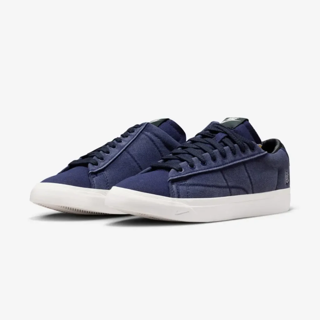 A pair of low-top navy blue sneakers featuring a minimalist canvas upper, matching navy laces, and a clean white midsole, shown from a three-quarter angle