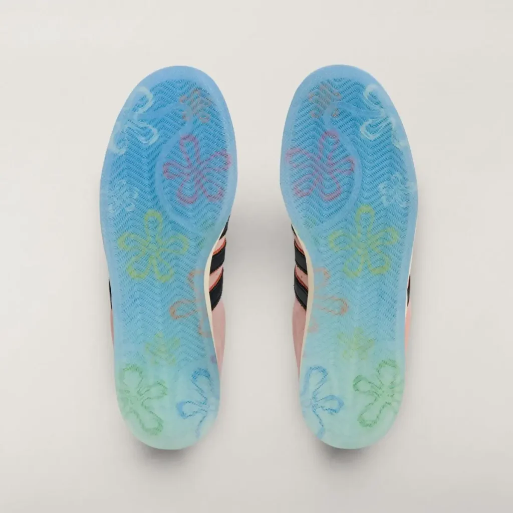Bottom view of the SpongeBob SquarePants x adidas Superstar “Patrick Star” sneakers showing translucent blue outsoles decorated with multicolor floral graphics inspired by Bikini Bottom, photographed on a light background