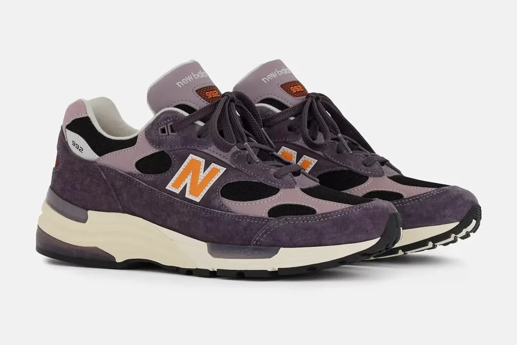 A pair of New Balance Made in USA 992 “Dark Ice Wine” sneakers featuring deep purple suede, lilac leather overlays, black mesh cut-outs, and orange-outlined “N” logos, set on an off-white midsole with black rubber outsoles