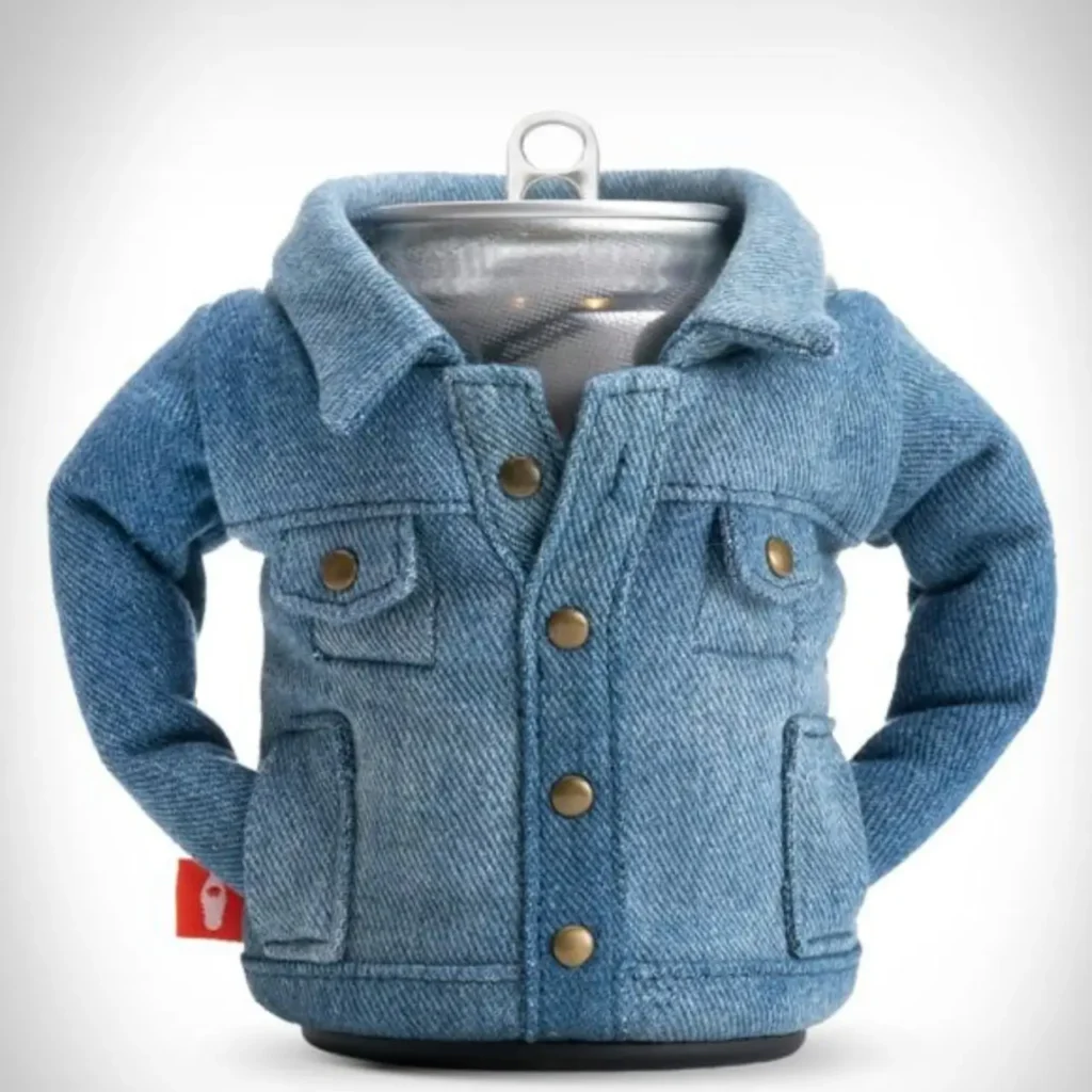 A beverage can wrapped in a miniature denim jacket–style Puffin Drinkware holder, complete with stitched seams, brass snap buttons, chest pockets, and structured sleeves, mimicking the look of classic blue jean outerwear