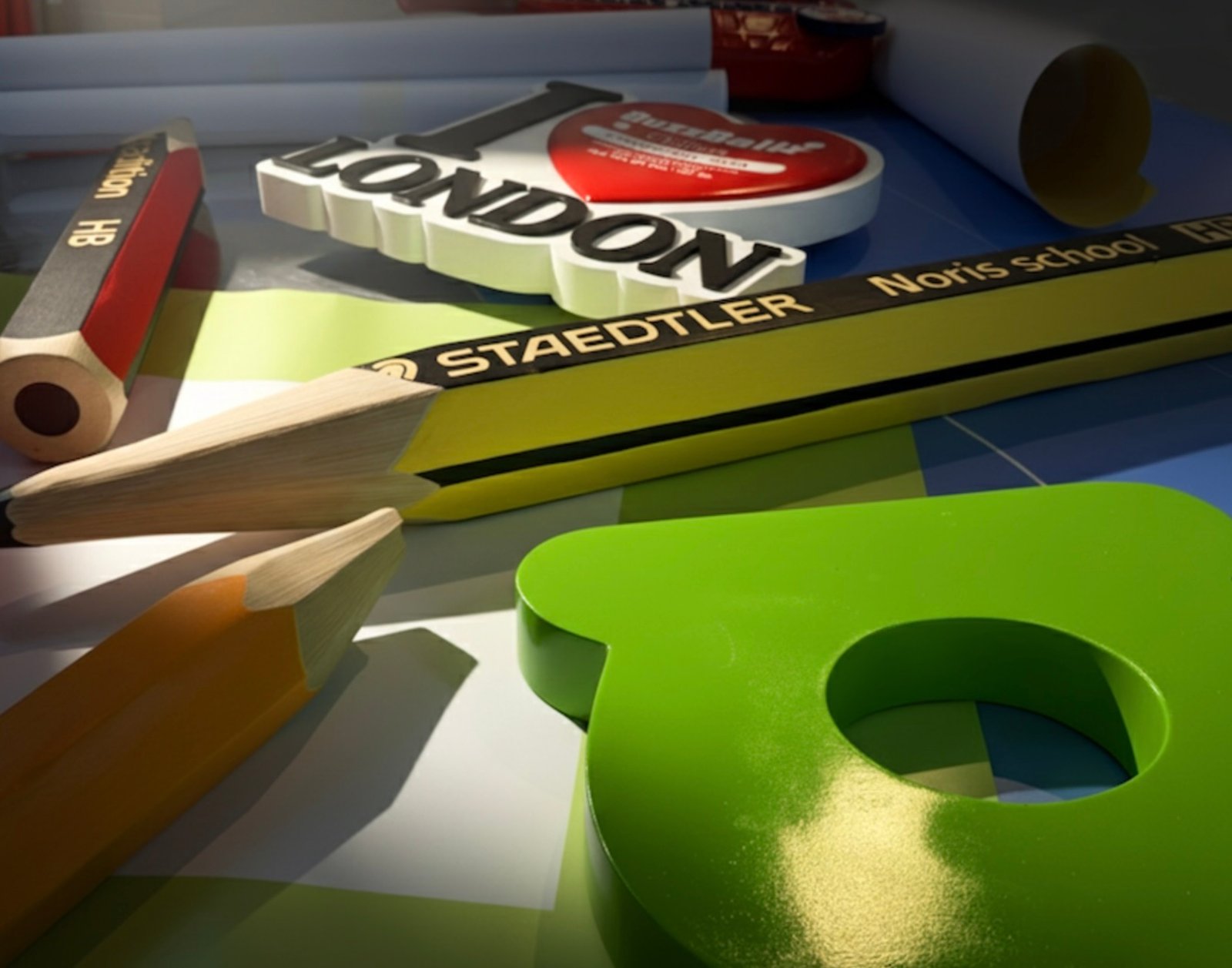 Close-up of childlike art materials including pencils, crayons, and cut-out letters arranged across a tabletop installation