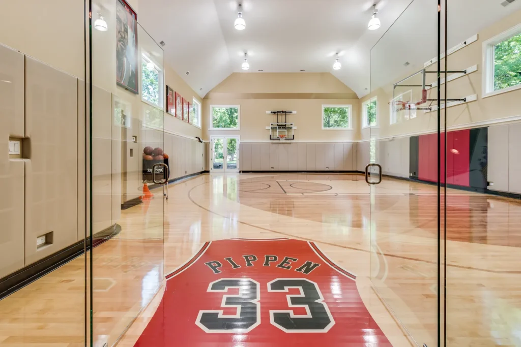Indoor basketball court inside Scottie Pippen’s Chicago mansion, featuring a polished hardwood floor, glass entry doors, and a large red Bulls-style Pippen 33 logo at center court