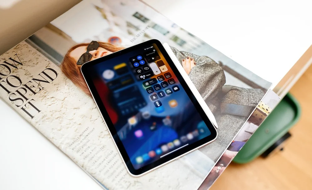 Tablet-sized Apple device concept shown unfolded on top of a magazine, displaying an iOS-style interface, illustrating rumors of a foldable iPhone that could expand into an iPad mini–like form factor