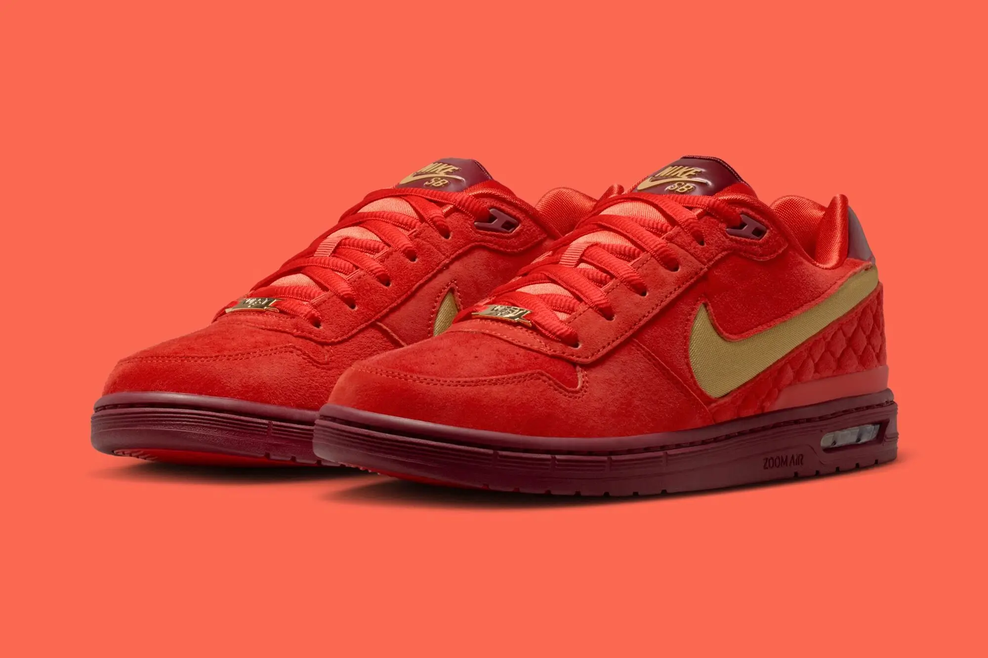 Nike SB P-Rod Zoom Air Low sneaker in a bold red suede finish with metallic gold Swoosh branding, shown in a side-angle pair shot against a coral background, highlighting the low-profile silhouette and visible Zoom Air cushioning