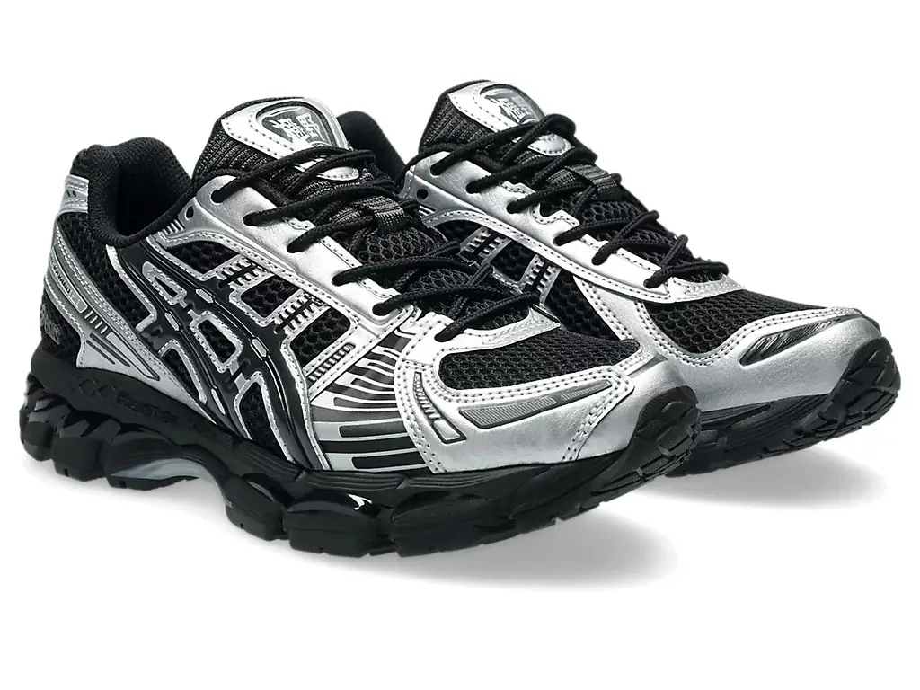 Carnival x ASICS GEL-Kayano 12.1 sneaker in black mesh with metallic silver overlays and tonal striping, featuring layered panel construction, black laces, and a sculpted cushioned sole unit shown in angled side profile