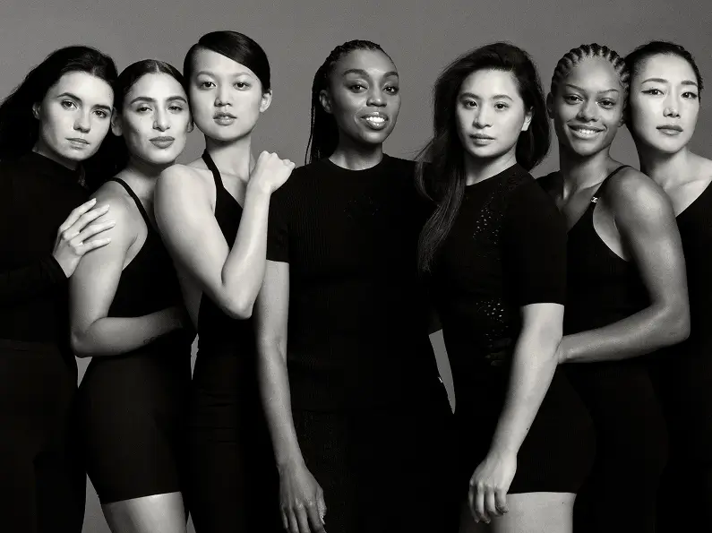 Seven female athletes stand closely together in a black-and-white Chanel Beauty campaign, wearing minimalist black outfits that emphasize strength, unity, and individuality through posture and expression