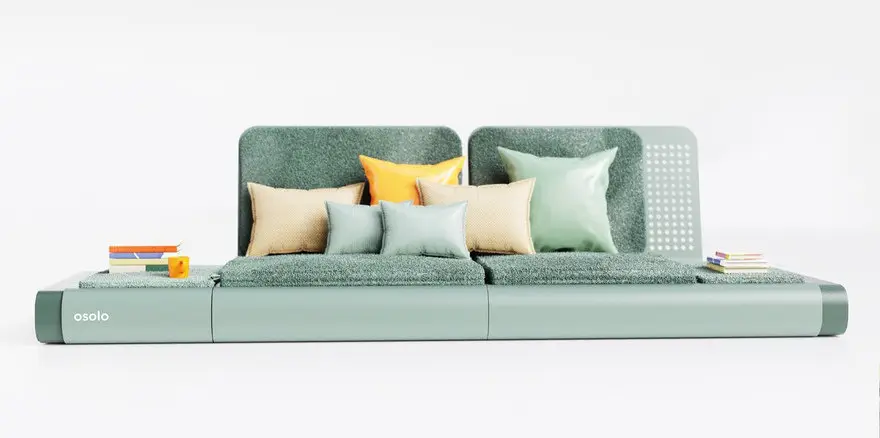 Front view of the Osolo sofa by Gökçe Nafak in a muted green finish, featuring a continuous folded metal base, low-profile textured cushions, and layered accent pillows in orange, beige, and green tones; styled with books and a small orange cup on the extended side platforms