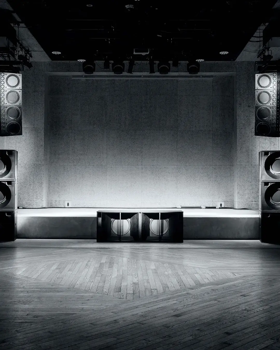 Interior of a minimalist electronic music venue featuring a wooden dance floor and large stacked sound system speakers designed for high-fidelity club audio