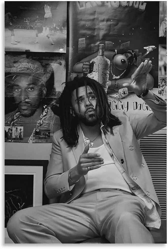 Portrait of J. Cole seated in a room surrounded by hip-hop posters and memorabilia, wearing a light suit and gesturing upward in a reflective black-and-white photograph.