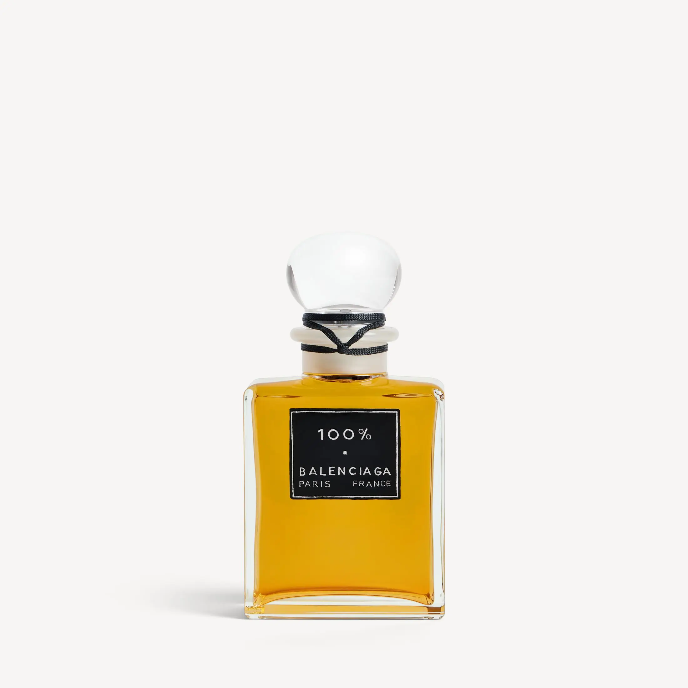 Front view of Balenciaga 100% perfume bottle with amber liquid, square glass design, black label reading “100% Balenciaga Paris France,” and a rounded glass stopper wrapped with a black cord
