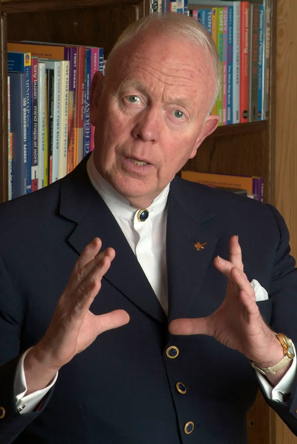 Tony Buzan speaking with hands raised in front of a bookshelf, illustrating mind mapping and radiant thinking concepts