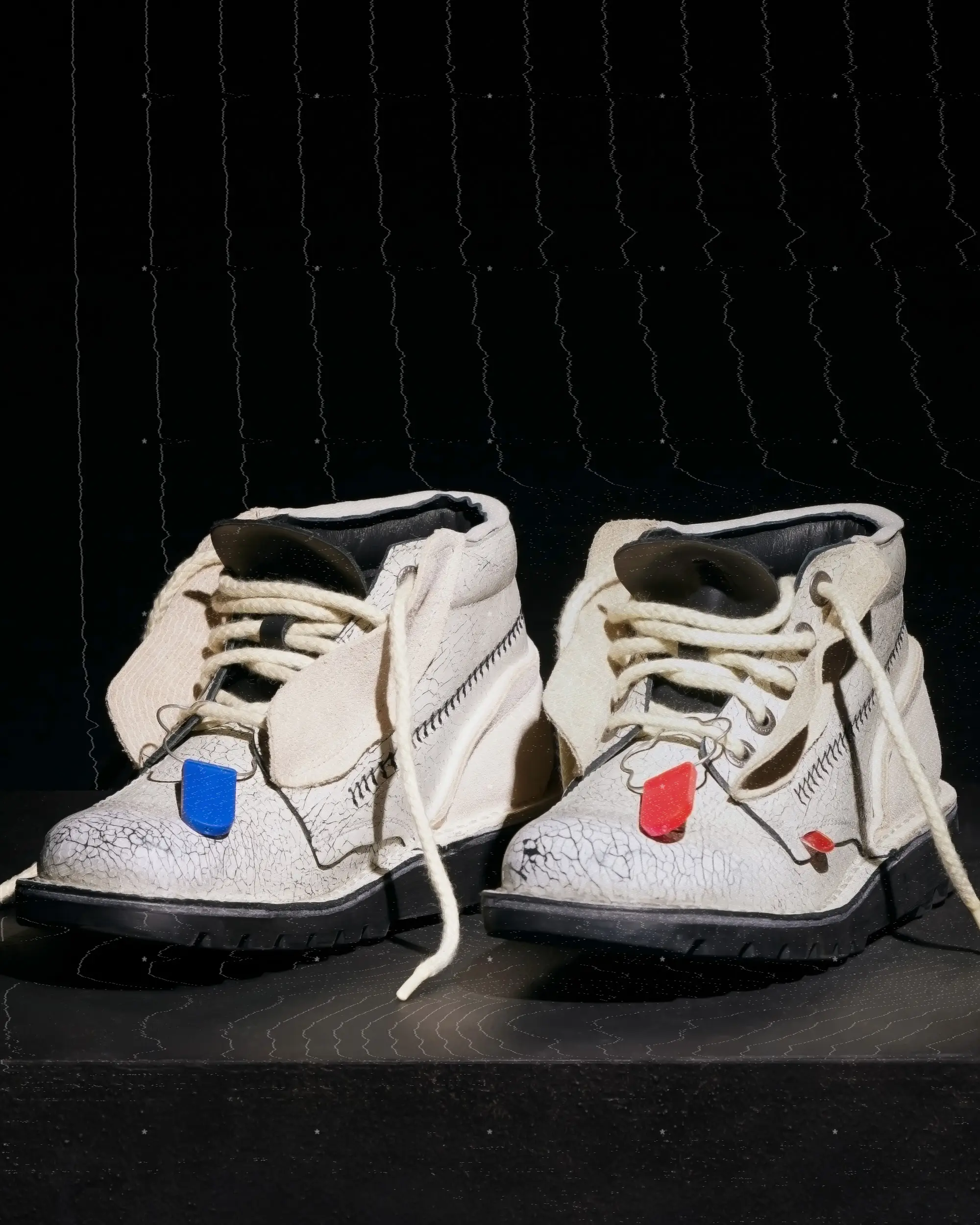 Cream crackled leather Kickers x A-COLD-WALL* limited-edition silhouette with rugged black lug sole, thick rope laces, exposed stitching, and signature red and blue lace tabs on a dark minimalist display