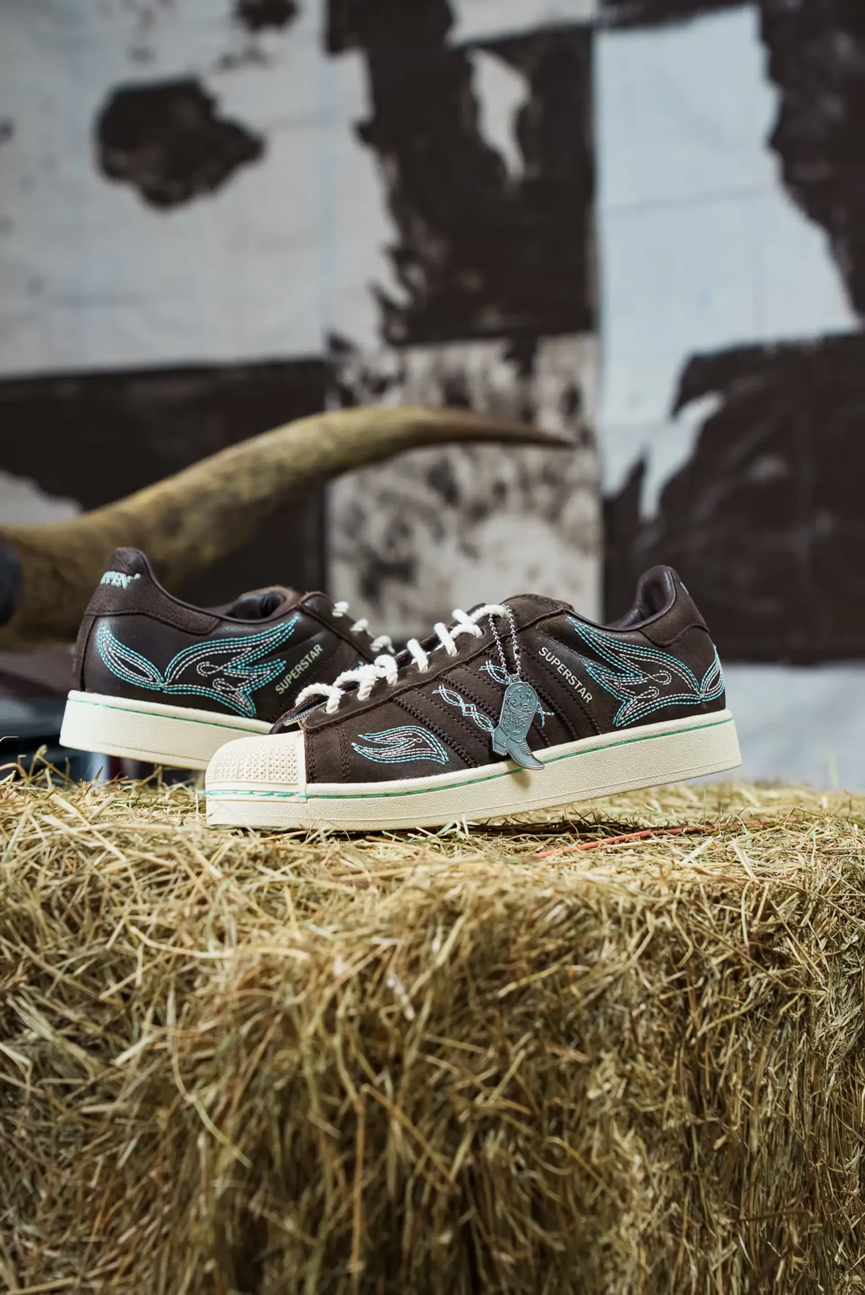 Side view of adidas Superstar “Lone Star Reppin’” brown leather sneakers with turquoise Western embroidery and shell toe displayed on a hay bale
