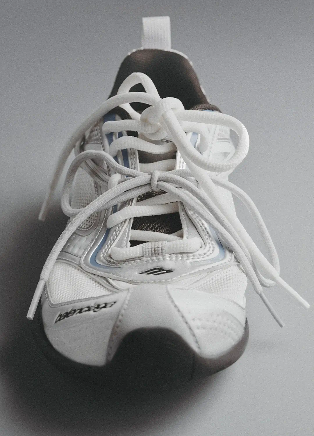 Front-facing view of the Balenciaga Radar Shoe in white, highlighting its intricate double lacing system layered over a breathable mesh upper, with subtle blue accents framing the eyelets; debossed Balenciaga branding appears along the side, while the streamlined toe shape and low-profile sole emphasize its lightweight, responsive design
