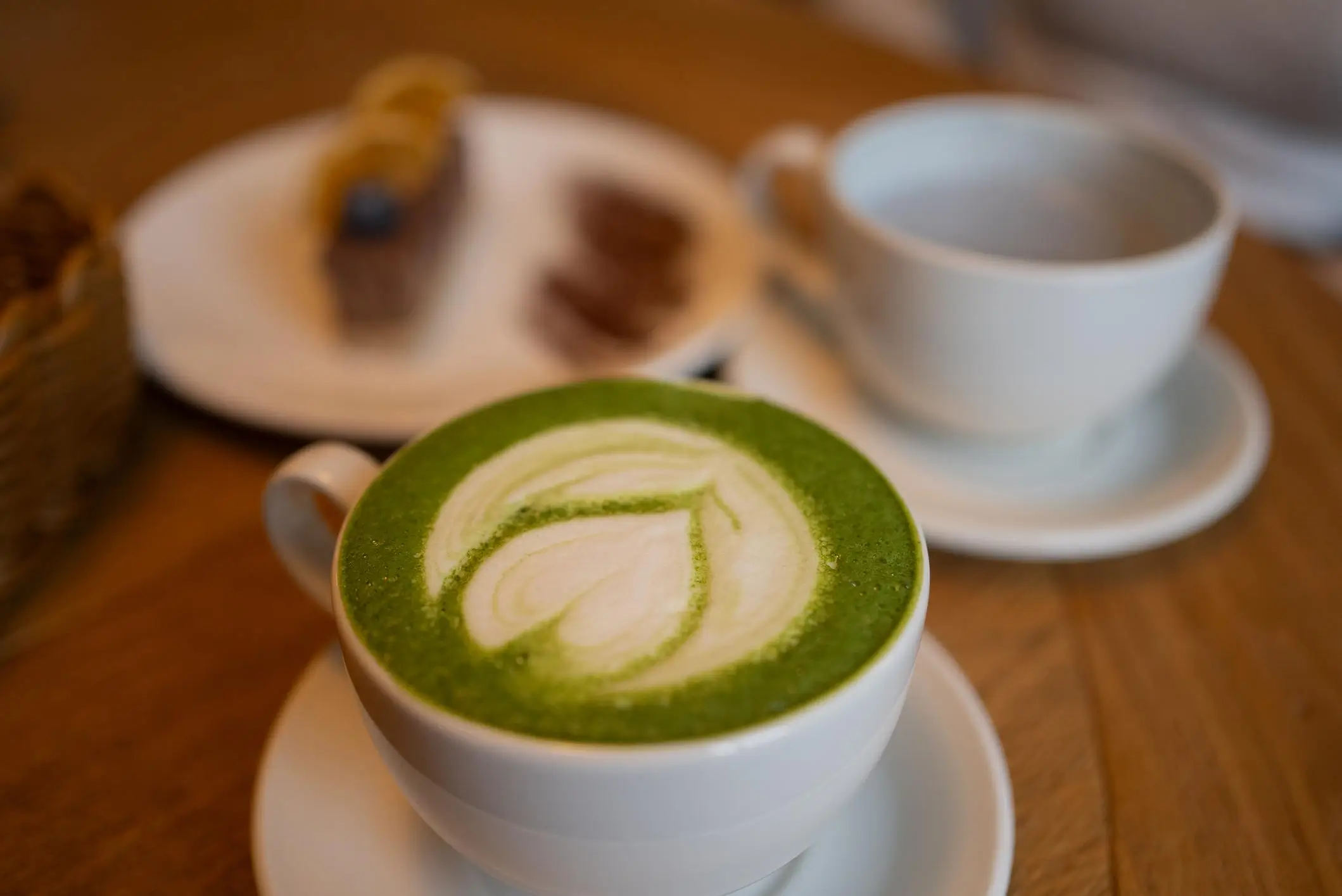 Minimalist scene showing freshly whisked matcha in a ceramic bowl with a bamboo chasen whisk resting inside, placed next to a small container of vibrant green matcha powder on a light stone surface, illustrating traditional Japanese matcha preparation