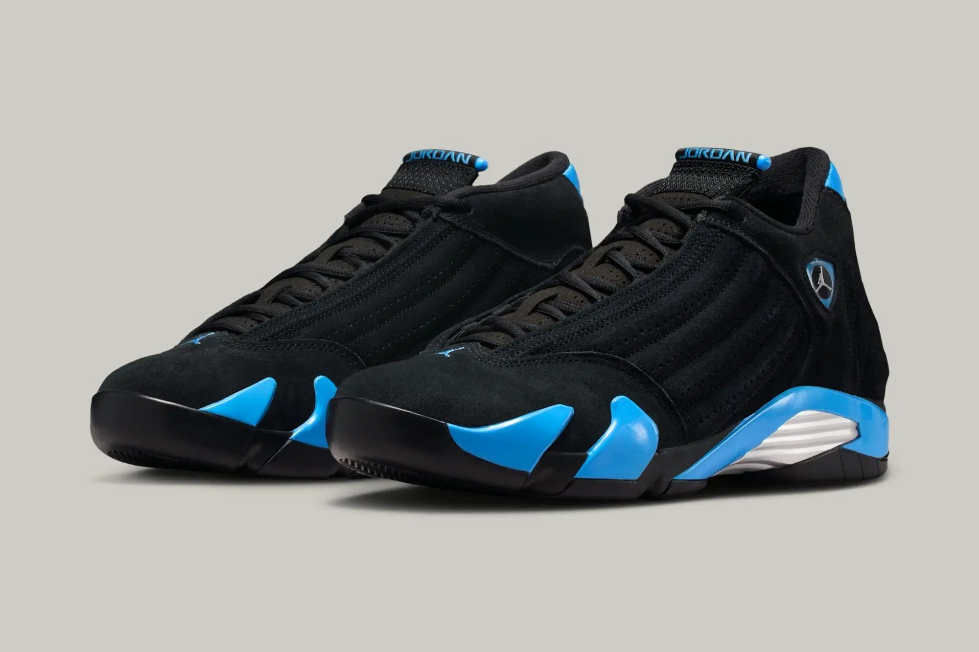 Pair of Air Jordan 14 “University Blue” sneakers shown in angled front view featuring black nubuck uppers, bright University Blue midsole accents, black laces, and the signature Ferrari-inspired Jumpman shield on the side