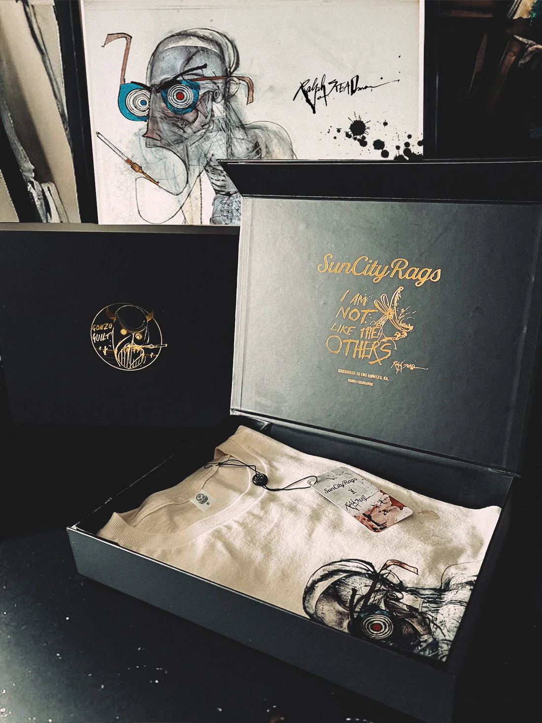 Limited edition Ralph Steadman Hunter S. Thompson memorial T-shirt presented in a premium Sun City Rags box set, featuring gold-embossed branding, Gonzo-themed artwork, and the illustrated skeletal portrait folded inside with branded tag and packaging