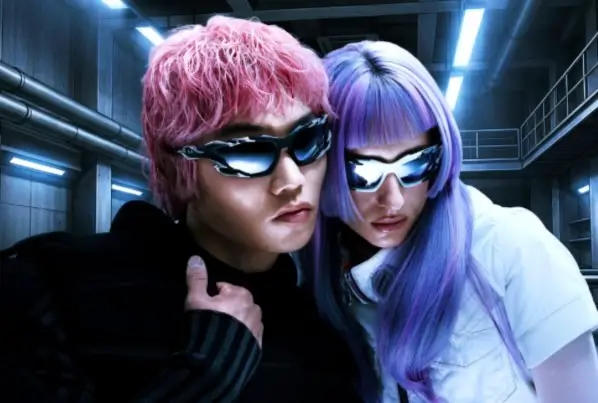 Two models pose closely together in an industrial, futuristic setting, both wearing reflective wraparound sunglasses with chrome-like finishes. One has short pink hair and a dark outfit, while the other has long lavender hair and a white top. Cool blue lighting and metallic surroundings enhance the sci-fi aesthetic, echoing themes of liquid metal and experimental design