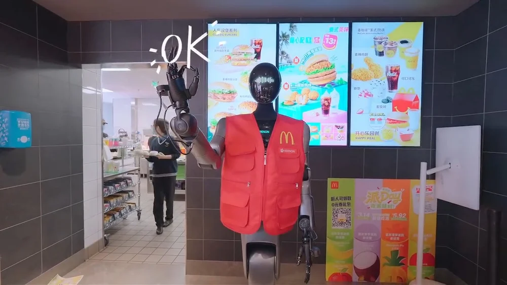 Humanoid robot in McDonald’s uniform positioned between kitchen and counter, signaling approval inside a Shanghai location
