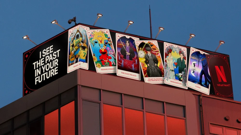 A large rooftop billboard displays a tarot-inspired campaign by Netflix, featuring illustrated cards referencing popular titles like Sesame Street, Bridgerton, and Lupin, alongside the phrase “I See the Past in Your Future” and a glowing red Netflix logo against a dusk sky