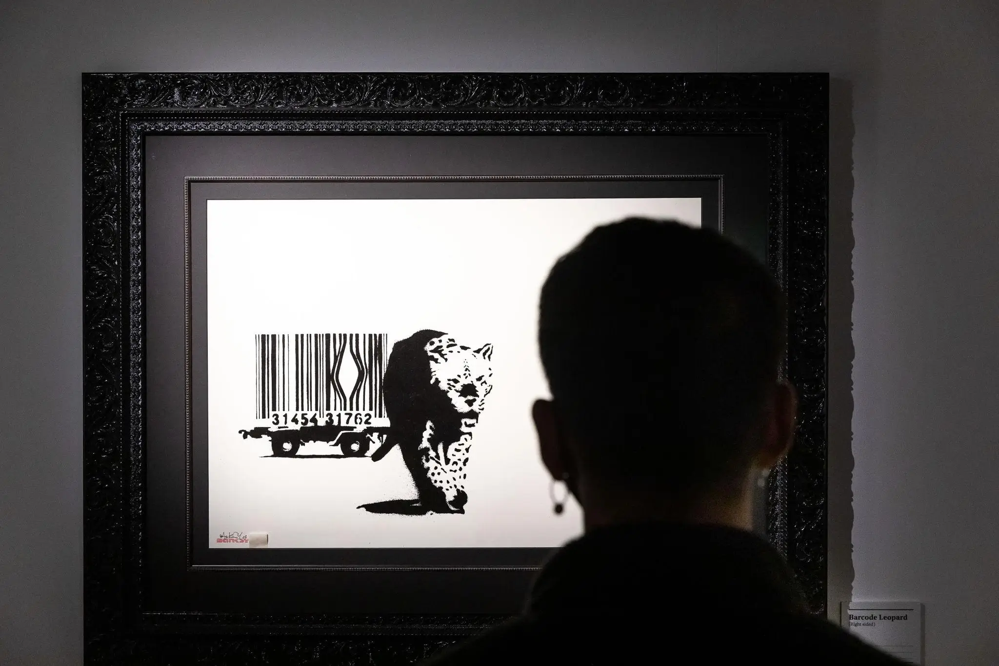 Gallery visitor viewing Banksy’s Barcode Leopard artwork framed on a wall