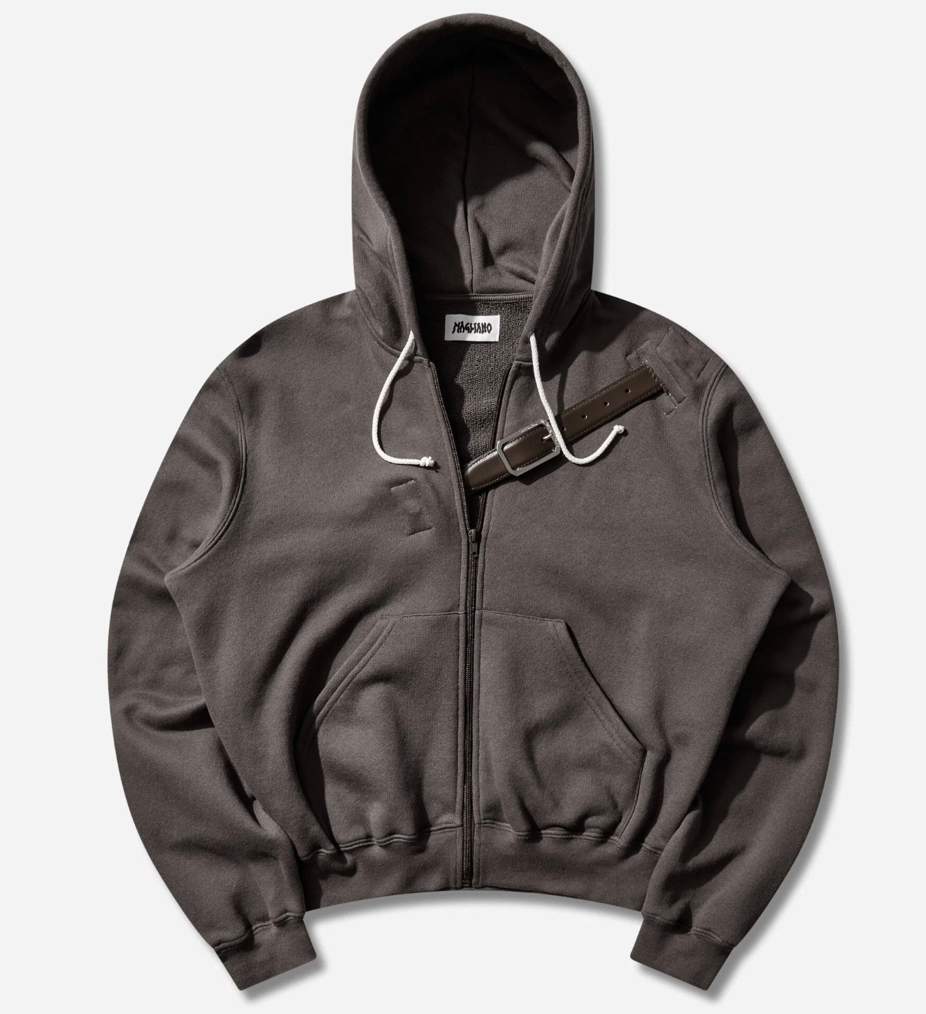 Magliano Provincia zip-up hoodie in brown cotton jersey featuring a front zipper closure, white drawstring hood, ribbed cuffs and hem, kangaroo pockets, subtle tonal chest detailing, and a dark leather strap with metal buckle accent across the upper chest, displayed against a light grey background