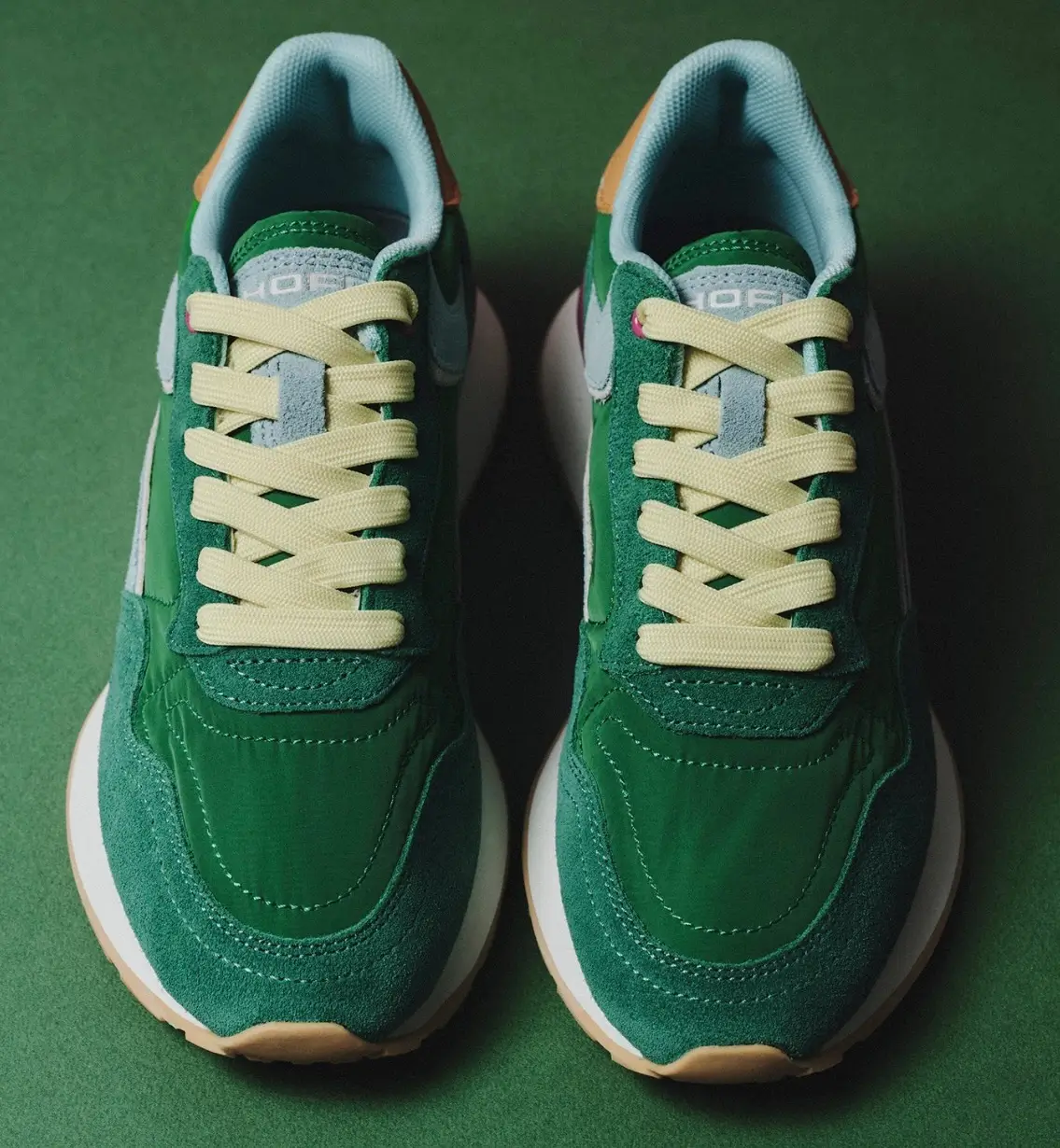 Top-down view of the HOFF City Dopamine Jade sneaker, featuring a rich green suede and leather upper, pastel mint panels, soft yellow laces, and a cream midsole against a green background