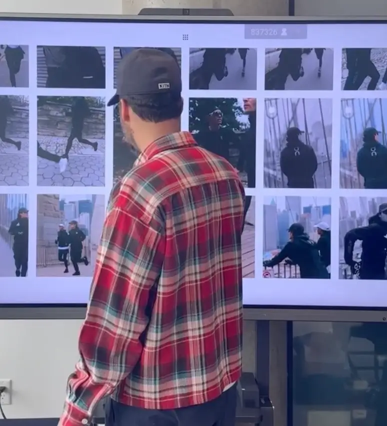 Ronnie Fieg wearing a Kith cap and red plaid shirt reviewing running imagery on a large screen during the development process of the Kith x On Running K-Tech performance shoe