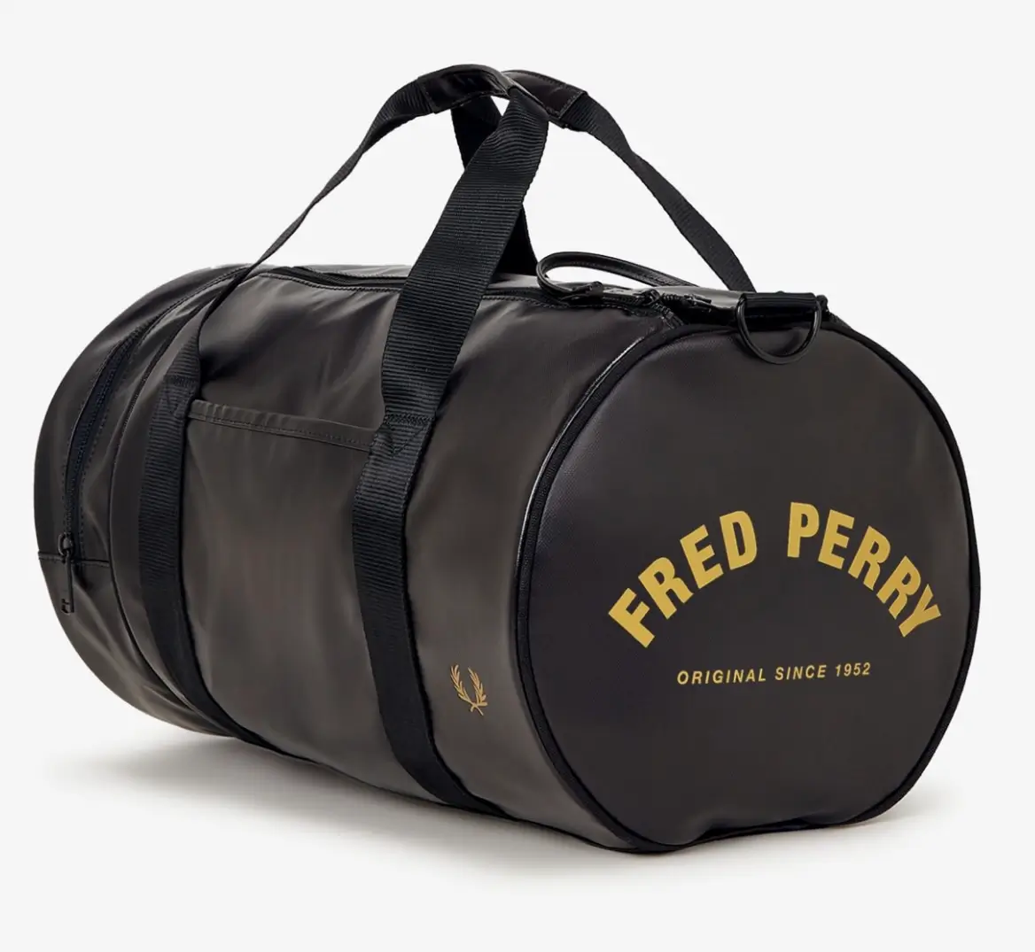Angled three-quarter view of the Fred Perry Tonal Barrel Bag L7260 showing the cylindrical silhouette, textured black finish with subtle sheen, dual black webbing carry straps, side zip pocket, gold laurel wreath logo on the body, and bold gold “FRED PERRY” branding across the circular end panel