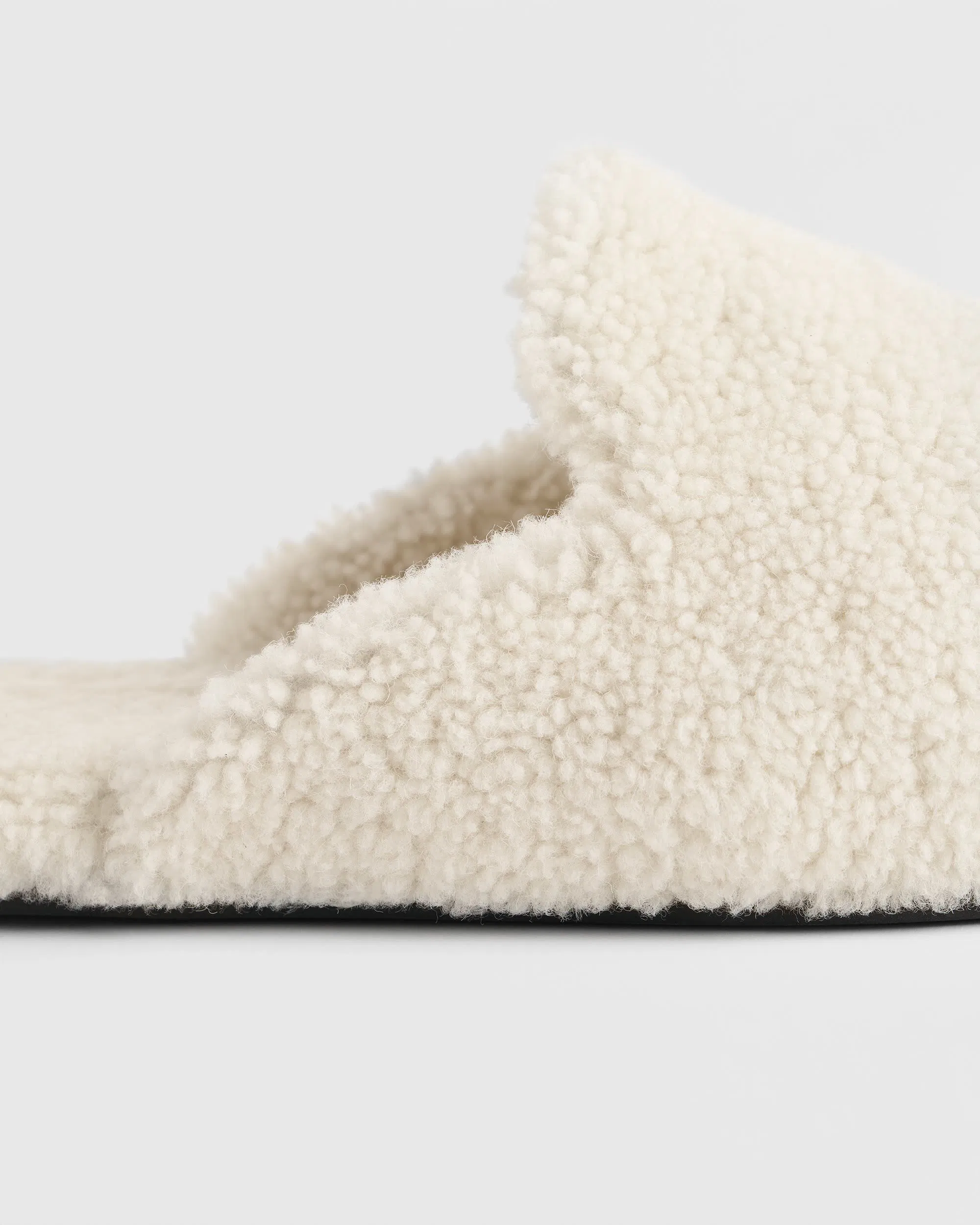 Close-up side detail of cream shearling Tekla slipper, highlighting dense wool texture, soft curved upper, and minimal black outsole edge