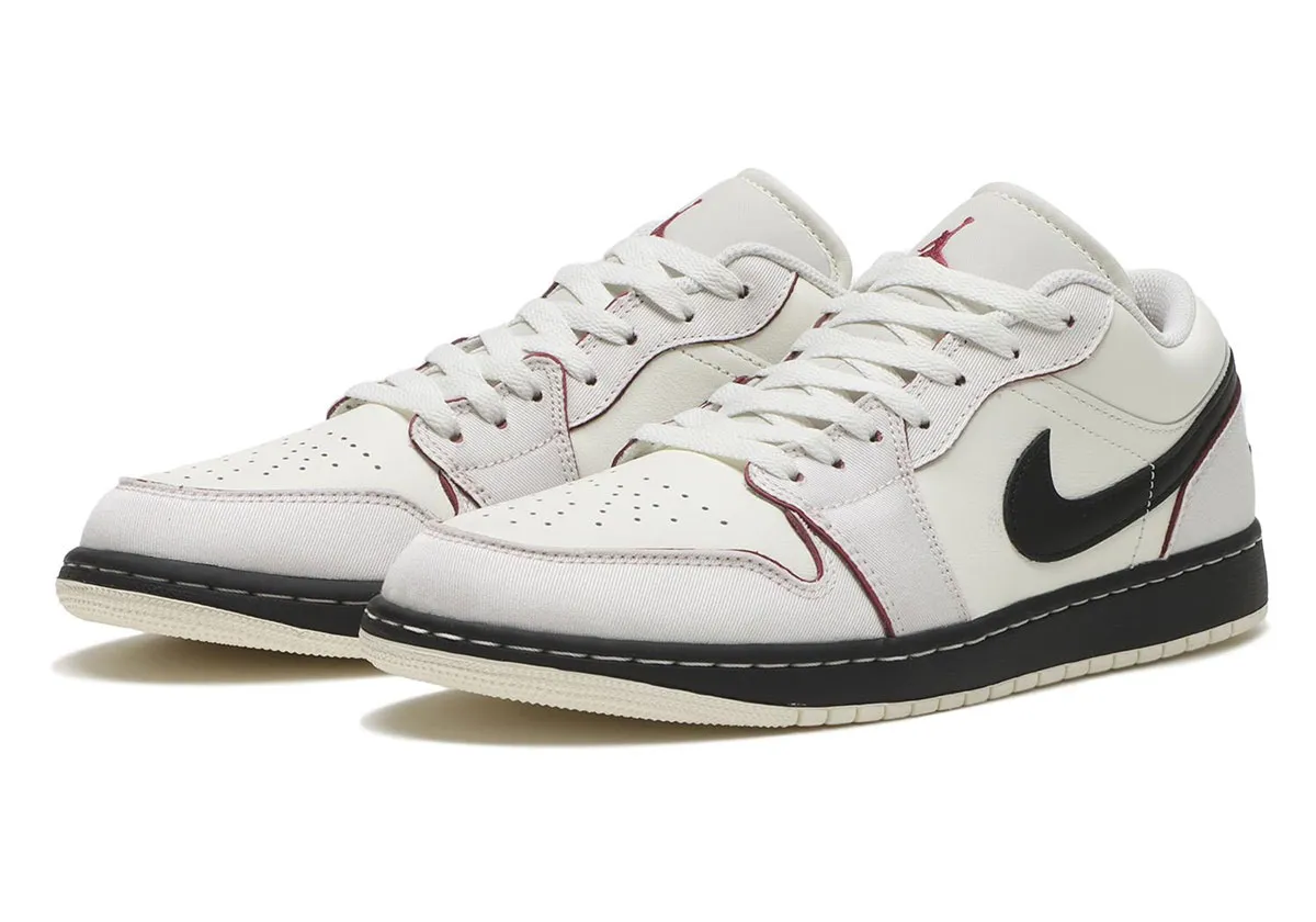 Pair of Air Jordan 1 Low “Sweet Beet” sneakers in Sail canvas and white leather, featuring black Swooshes, red piping accents, perforated toe boxes, and black midsoles with off-white outsoles, shown from a front angled view