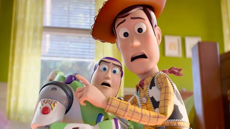 Woody and Buzz Lightyear look alarmed as they lean forward inside a brightly lit child’s bedroom, their expressions tense while Woody points toward something off-screen, suggesting a moment of sudden concern or discovery