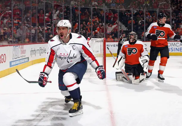 Alex Ovechkin celebrates after scoring a goal for the Washington Capitals, skating forward with arms outstretched as Flyers goalie and defenders react behind him in a packed arena