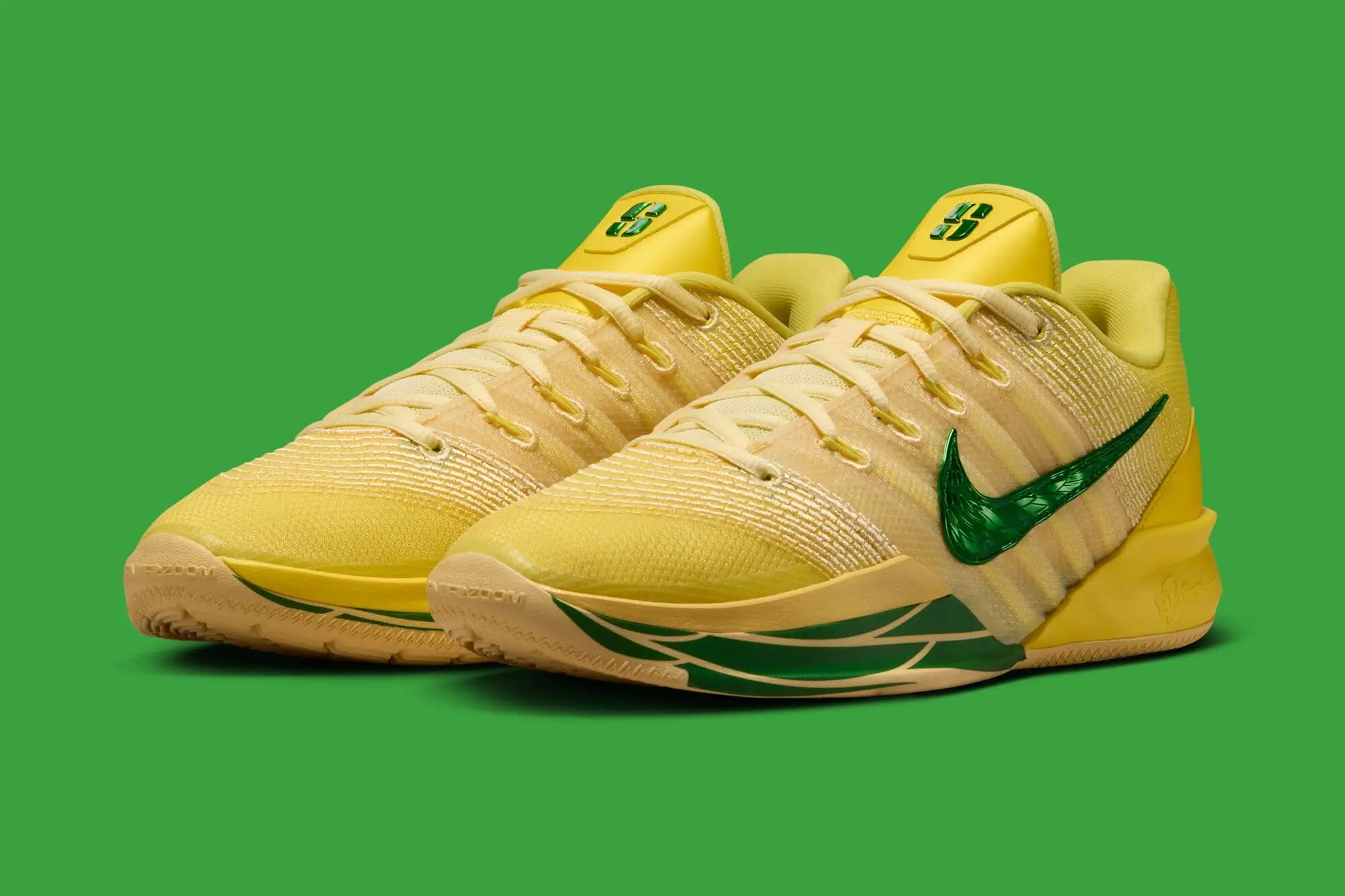 Pair of Nike Sabrina 3 “Oregon Ducks” basketball shoes in bright yellow with glossy green Swooshes, cream laces, and gum outsoles, shown on a green background