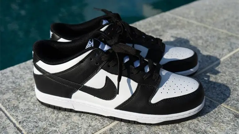 Nike Dunk Low “Panda” shoe in black and white leather, photographed side-by-side on a stone surface near a pool, with clean uppers, black Swooshes, and neatly laced tongues in natural outdoor lighting