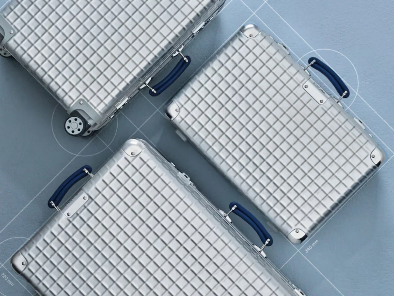 Flat-lay of multiple RIMOWA Classic Aluminium Grid suitcases arranged on a blueprint-style surface, highlighting embossed grid-pattern shells, polished aluminum corners, and blue leather handles with visible structural detailing