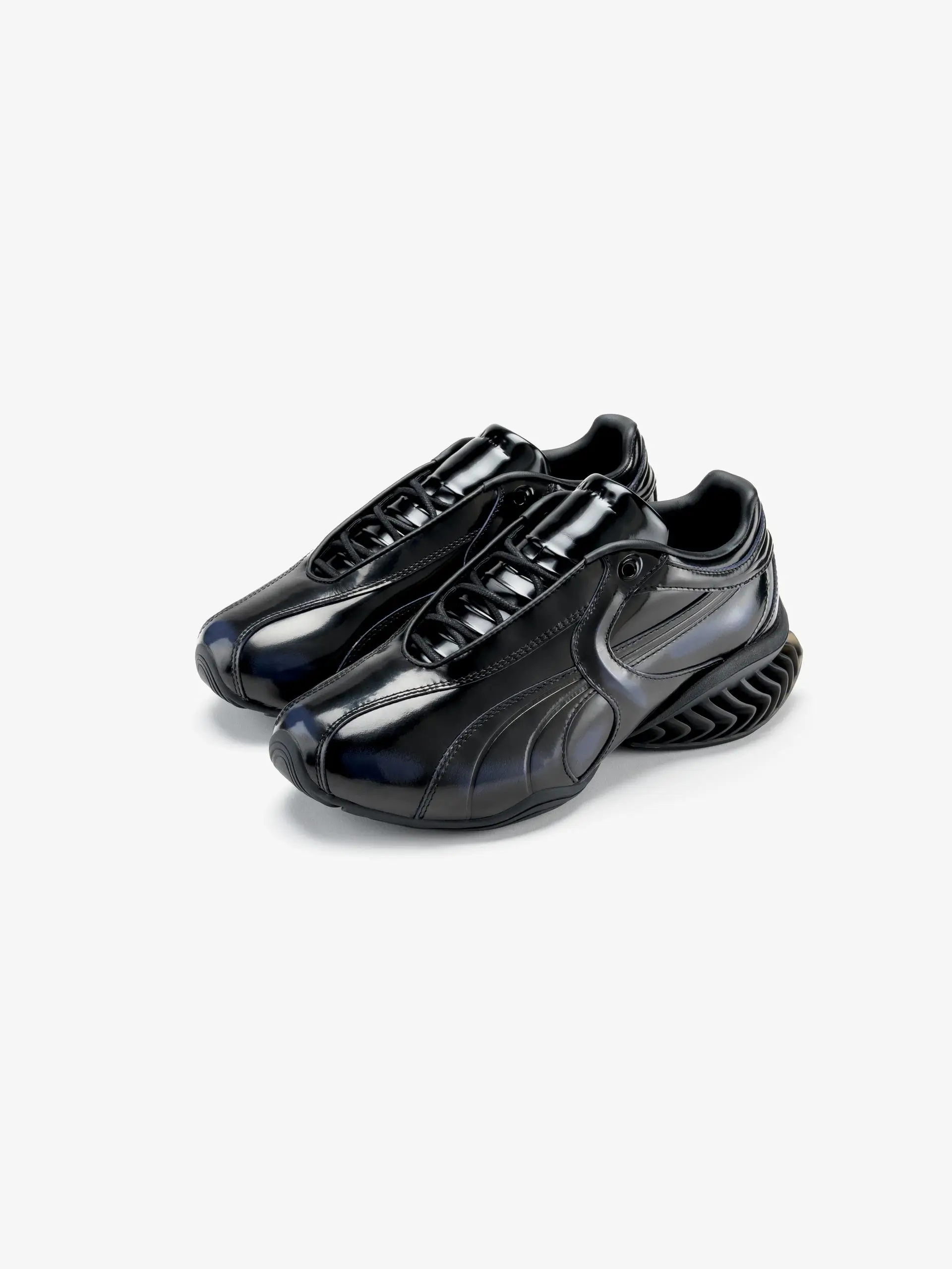 lossy black PUMA x J.L-A.L shoes in a sculptural low-profile silhouette, featuring a smooth patent leather upper, concealed lacing system, and futuristic CELL-inspired sole against a clean neutral background