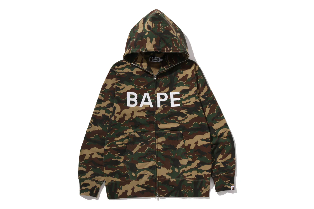 BAPE woodland camo zip-up hoodie with bold white BAPE logo on chest, featuring front pockets and hooded streetwear design