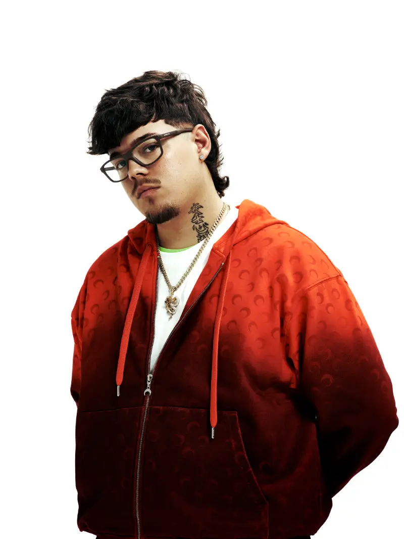 Saiko wearing Arnette optical glasses with a red zip-up hoodie and gold chain against a clean studio background