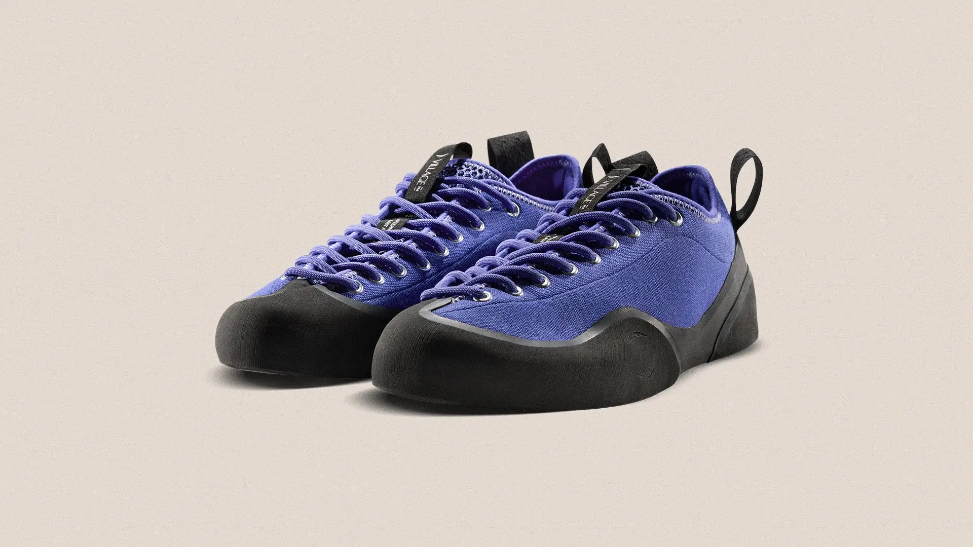 Three-quarter angled view of a pair of VILLAGE PM 1PM sneakers in natural purple canvas with sculpted black rubber soles and toe caps, tonal laces with metal eyelets, and rear pull tabs, placed on a neutral studio background